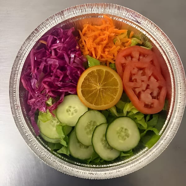Colorful Jamaican side salad with lettuce, red cabbage, carrots, tomatoes, cucumbers, and an orange slice.