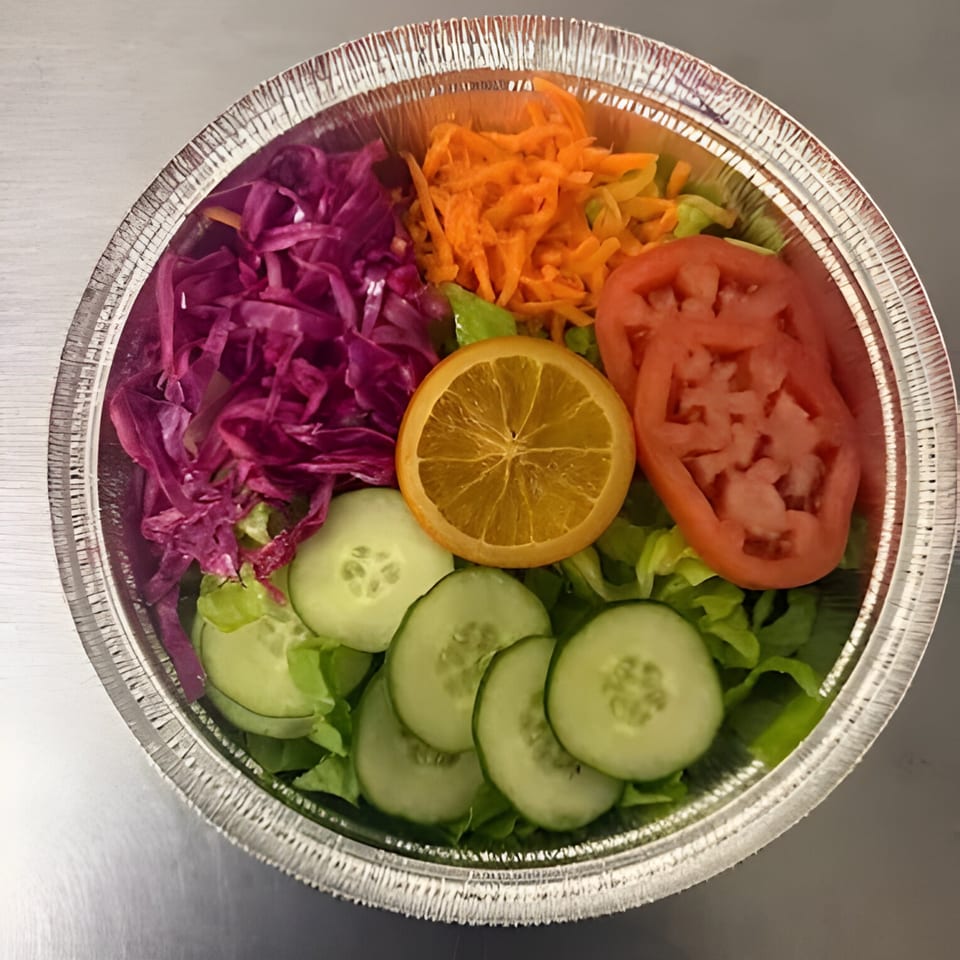 Colorful Jamaican side salad with lettuce, red cabbage, carrots, tomatoes, cucumbers, and an orange slice.