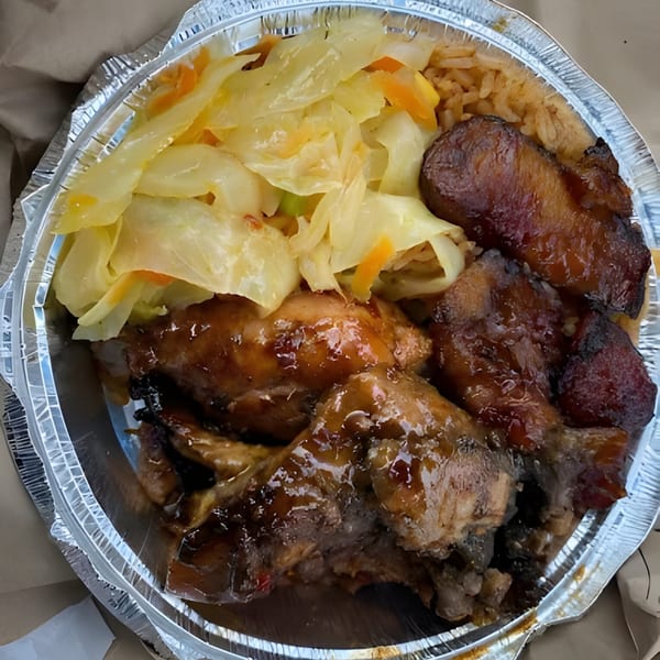 A Jamaican meal in a foil container with glazed chicken, rice, plantains, and cabbage.