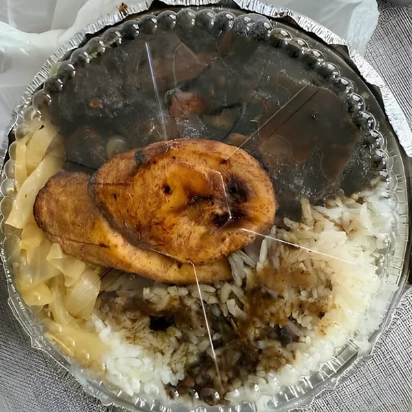 A Jamaican meal in a takeout container with rice, plantains, and dark stewed meat.