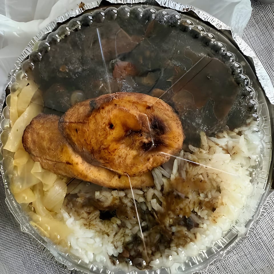 A Jamaican meal in a takeout container with rice, plantains, and dark stewed meat.